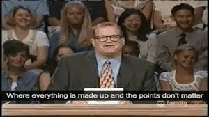 Man in suit and glasses speaks at a podium on TV, with audience behind him and subtitle: Where everything is made up...