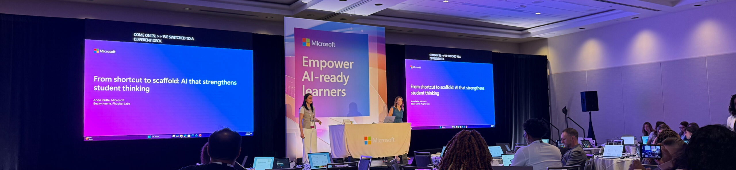 Microsoft conference stage with two presenters and screens reading From shortcut to scaffold: AI that strengthens student thinking and Empower AI-ready learners
