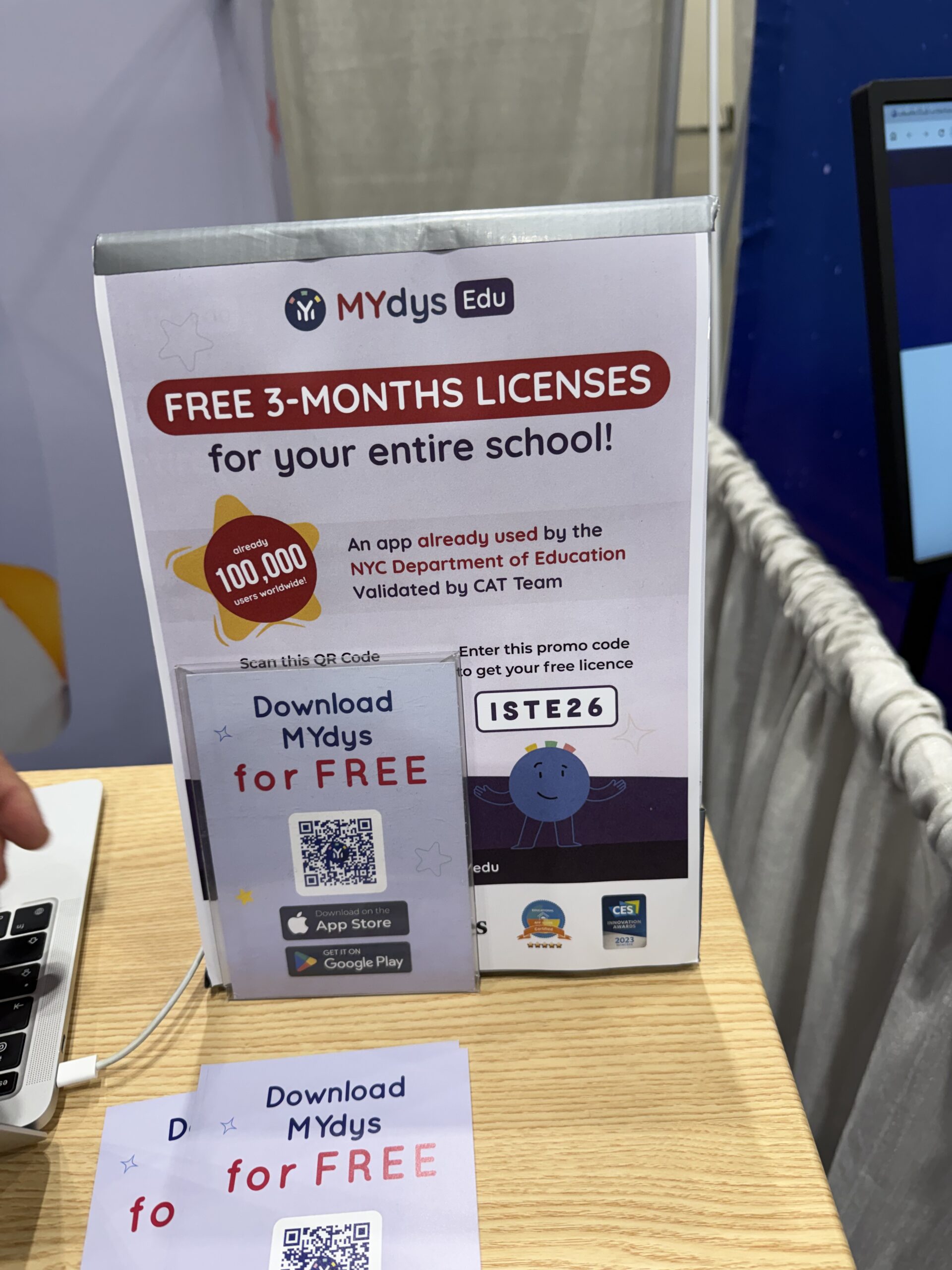 MYdus Edu booth sign offering free 3-month school licenses, with QR code, promo code ISTE26, and app download cards on a table