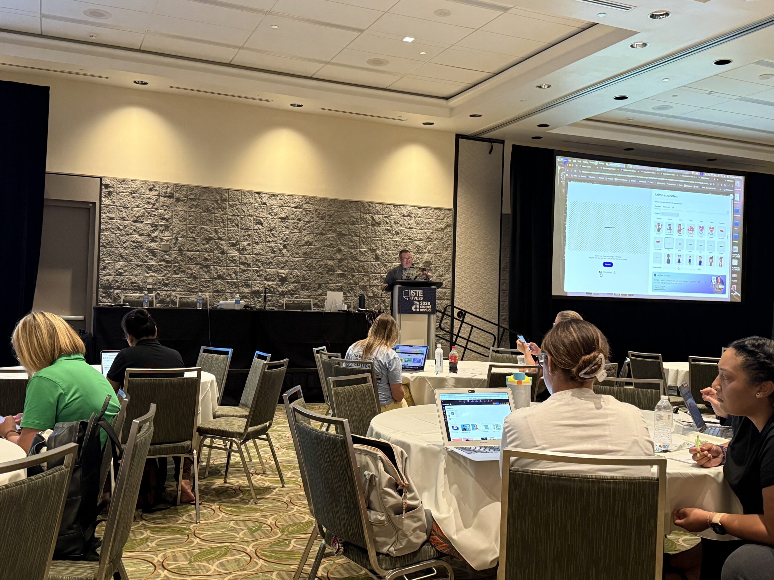 Conference workshop with presenter at podium, attendees on laptops, and projected slide reading Animate characters and ISTE LIVE 2026.