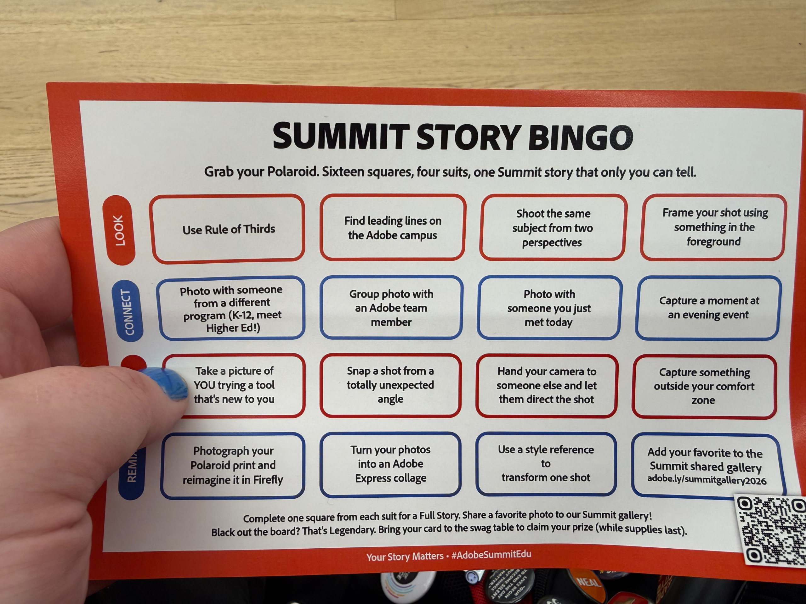 Hand holds a Summit Story Bingo card on a wooden table, with photo challenge boxes, bold title, and a QR code.